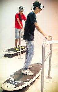 Jovens usam óculos de realidade aumentada 3D, com base em celular em simulador de prancha de surfe. (Foto: George Campos/USP Imagens)
