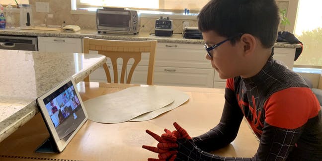Criança assisti aula online vestido de homem aranha. Crédito: Edsurge